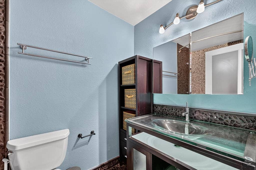 Vessel sink with a glass countertop, wood-finish vanity, and integrated shelving