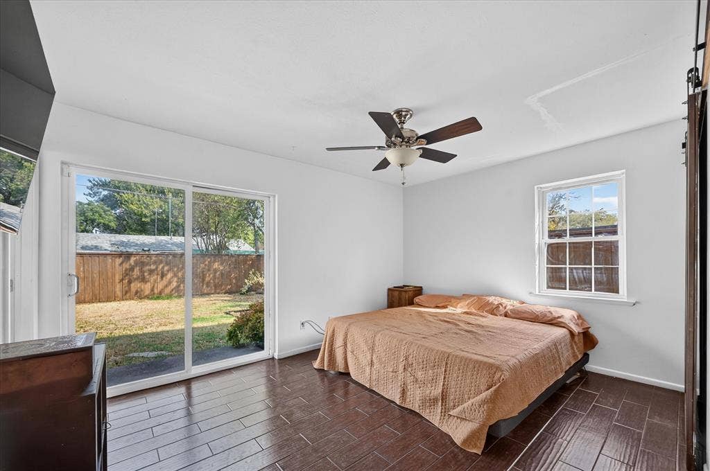 Wood-finish flooring, ceiling fan, and sliding glass door leading to a fenced yard