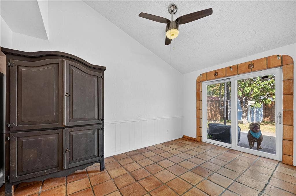 Terracotta-style floor tiling, vaulted ceiling, sliding glass doors, and a ceiling fan with integrated lighting