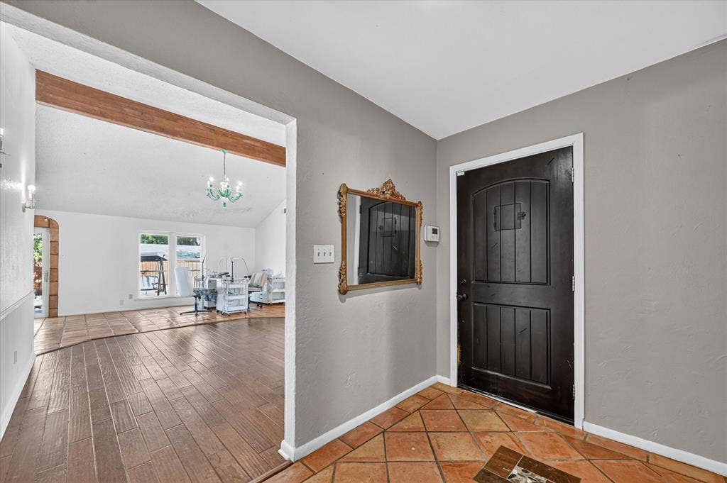 Archway with exposed wood beam, vaulted ceiling, wood-finish flooring, and a decorative chandelier