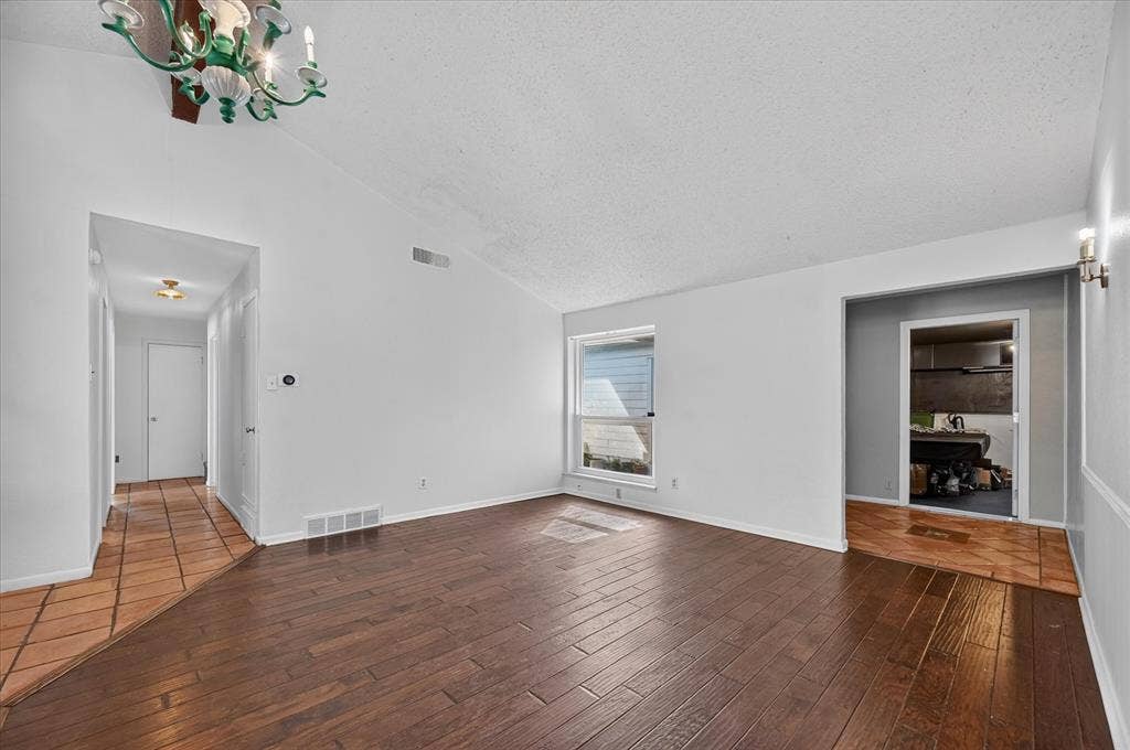 Vaulted ceiling, wood-finish flooring, single window, and a decorative chandelier