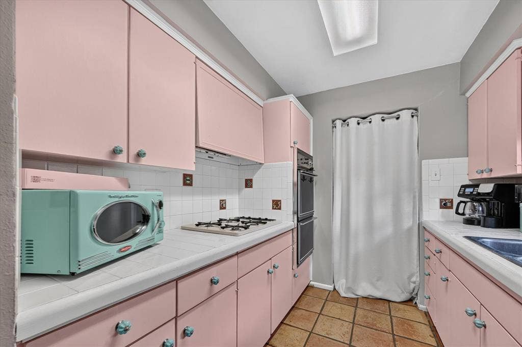Galley kitchen with pink cabinetry, tile flooring, tile countertops, and a double wall oven