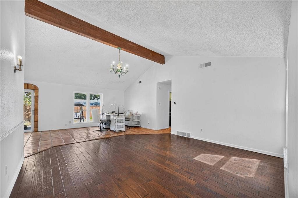 Vaulted ceiling with an exposed wood beam, wood-finish flooring, and a decorative chandelier