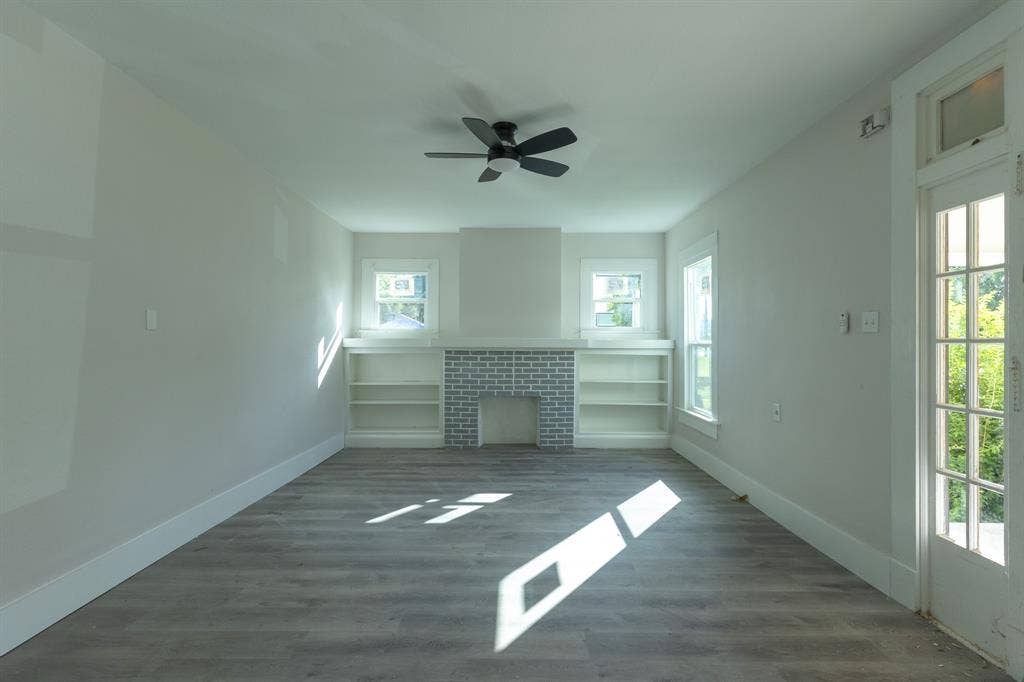 1702 Ethel Avenue, Waco, TX 76707 Bright and airy sunroom featuring expansive windows flooding the space with natural light, dark wood-finish flooring throughout, built-in shelving with brick accent wall, ceiling fan, and glass French doors opening to outdoor spaces
