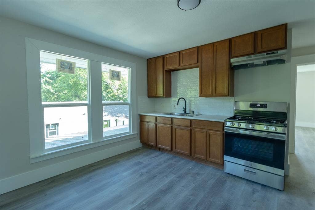 1702 Ethel Avenue, Waco, TX 76707 Wood-finish flooring, white subway tile backsplash, stainless steel gas range, brown shaker-style cabinetry, and a black gooseneck faucet