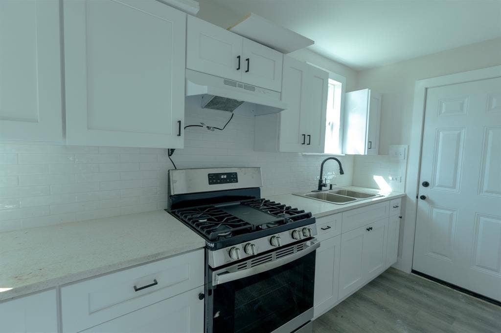 1702 Ethel Avenue, Waco, TX 76707 White shaker-style cabinetry with matte black hardware, stainless steel gas range, white subway tile backsplash, light-toned countertops, and a dual basin sink with a matte black faucet