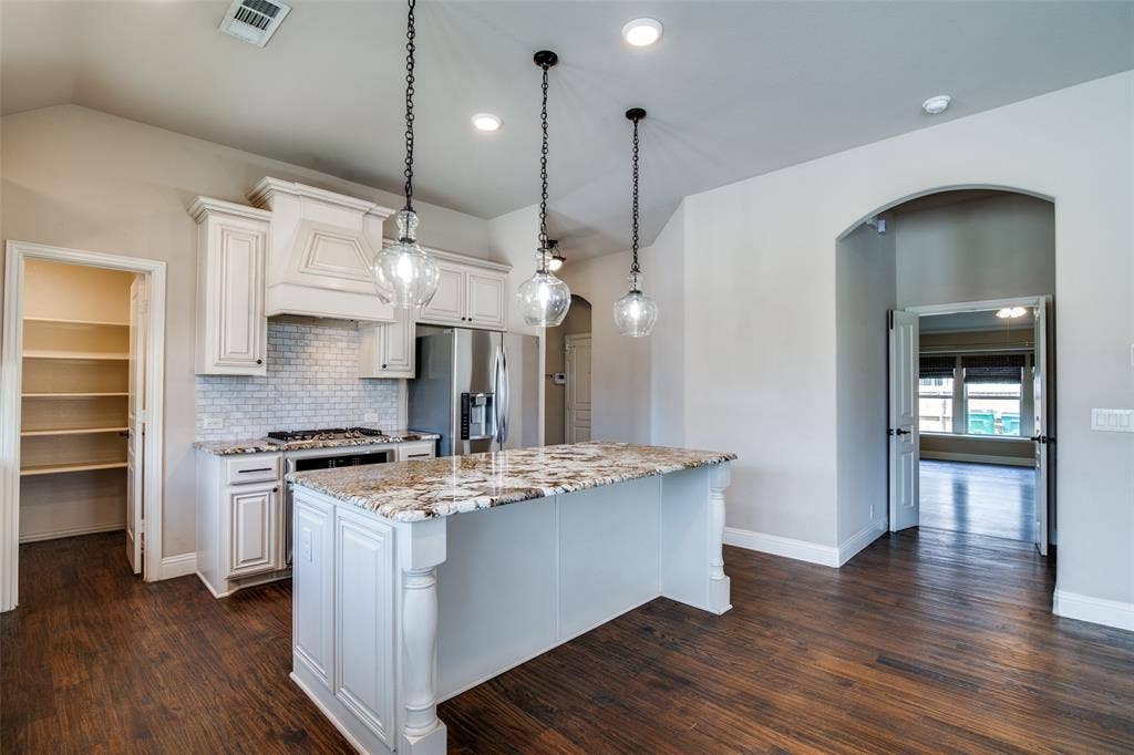 1813 Chadwick Lane, Forney, TX 75126 Gourmet kitchen featuring a large central island with a stone-finish countertop, white cabinetry, integrated stainless-steel appliances, and a tiled backsplash