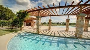 1813 Chadwick Lane, Forney, TX 75126 Resort-style outdoor entertaining space featuring a sparkling saltwater pool with sun-lounging deck, wood-lattice pergola overhead providing dappled shade, and stone column supports