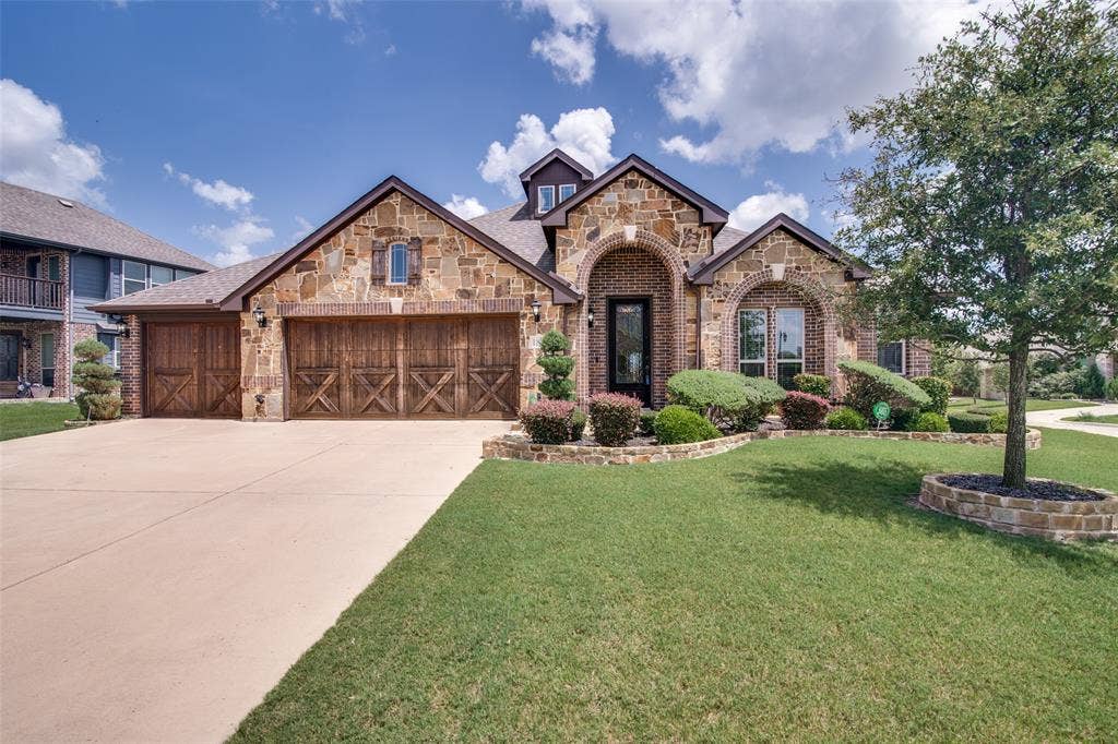 1813 Chadwick Lane, Forney, TX 75126 Stone and brick exterior with arched entryway, wood-finish garage doors, and established landscaping