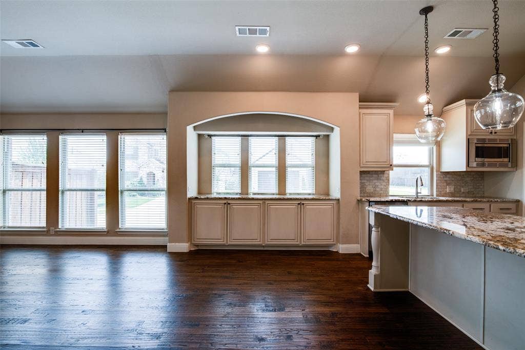 1813 Chadwick Lane, Forney, TX 75126 Open-concept living and kitchen featuring dark wood-finish flooring, custom cabinetry with arched architectural detailing, granite countertops, stainless steel appliances, and pendant lighting