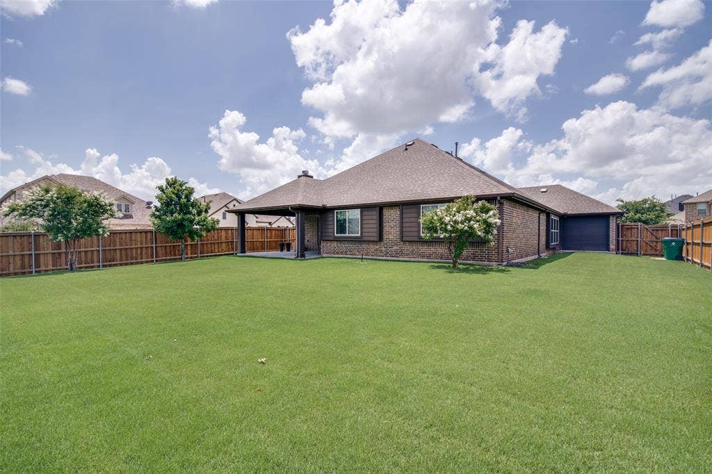 1813 Chadwick Lane, Forney, TX 75126 Expansive backyard featuring a manicured lawn, wood fencing, covered patio, and brick exterior