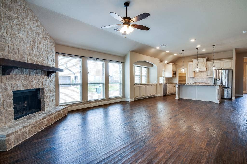 1813 Chadwick Lane, Forney, TX 75126 Open-concept living space featuring hardwood flooring throughout, a stone fireplace with black surround, and abundant natural light from multi-pane French doors and windows