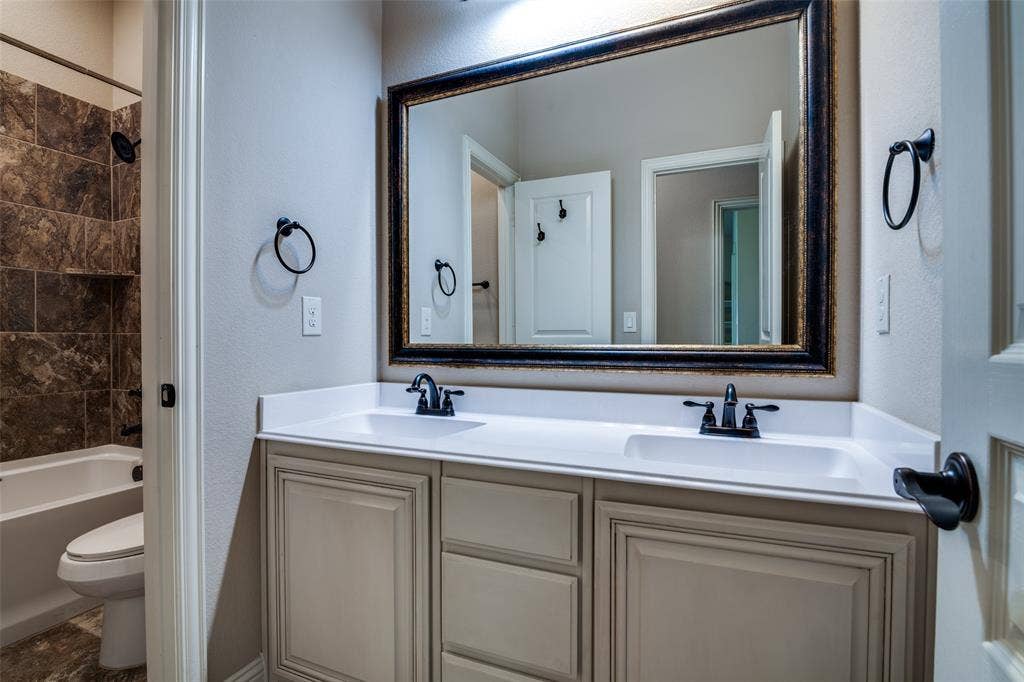 1813 Chadwick Lane, Forney, TX 75126 Dual vanity with white countertop and integrated sinks, framed mirror, matte black fixtures, built-in bathtub with shower, and tiled surround