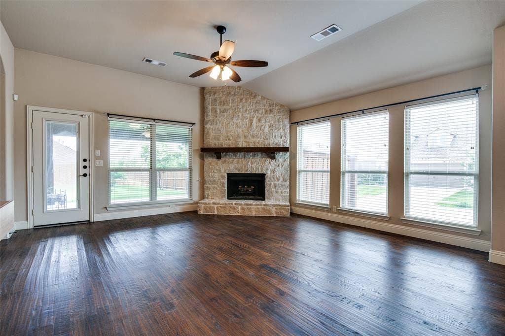 1813 Chadwick Lane, Forney, TX 75126 Vaulted ceiling with a ceiling fan, stone-clad corner fireplace with a wood mantle, rich wood-finish flooring, and multiple windows