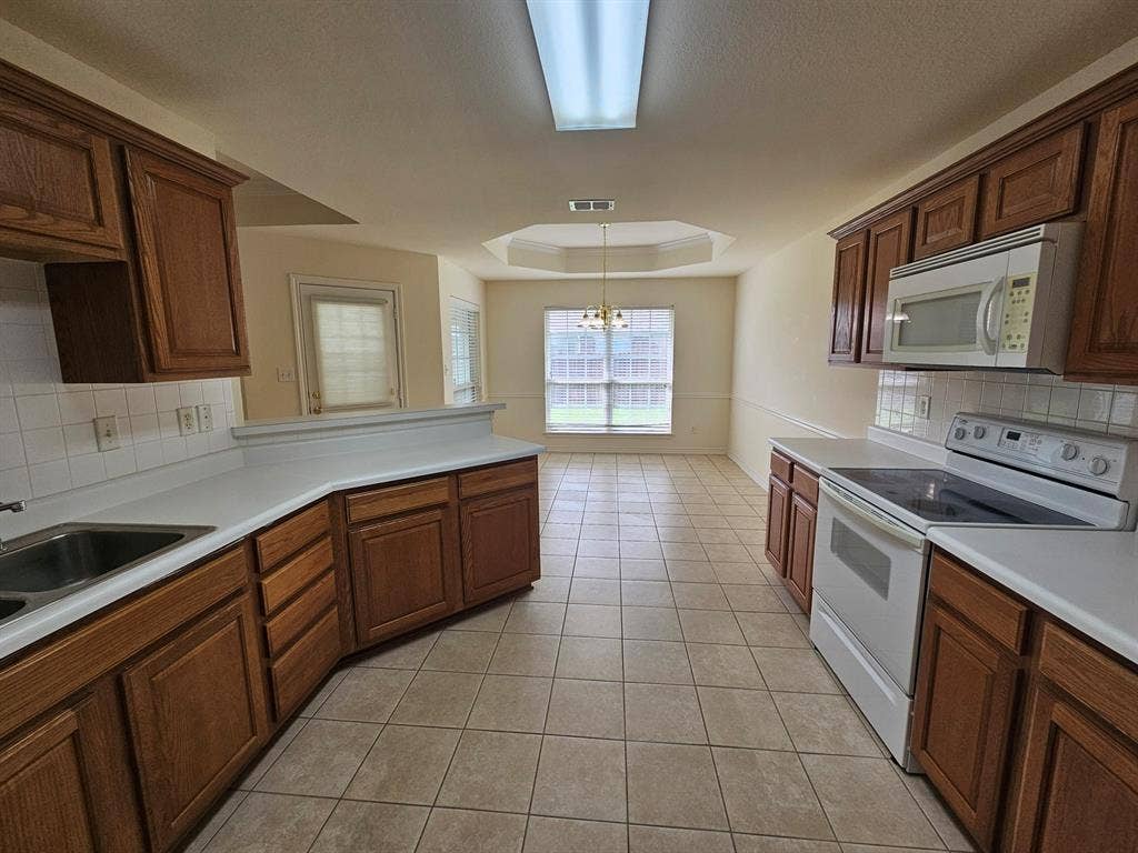 1521 Rice Road, #Z-101, Tyler, TX 75703 Tile flooring throughout, tray ceiling with crown molding, chair rail molding, wood cabinetry, and white appliances