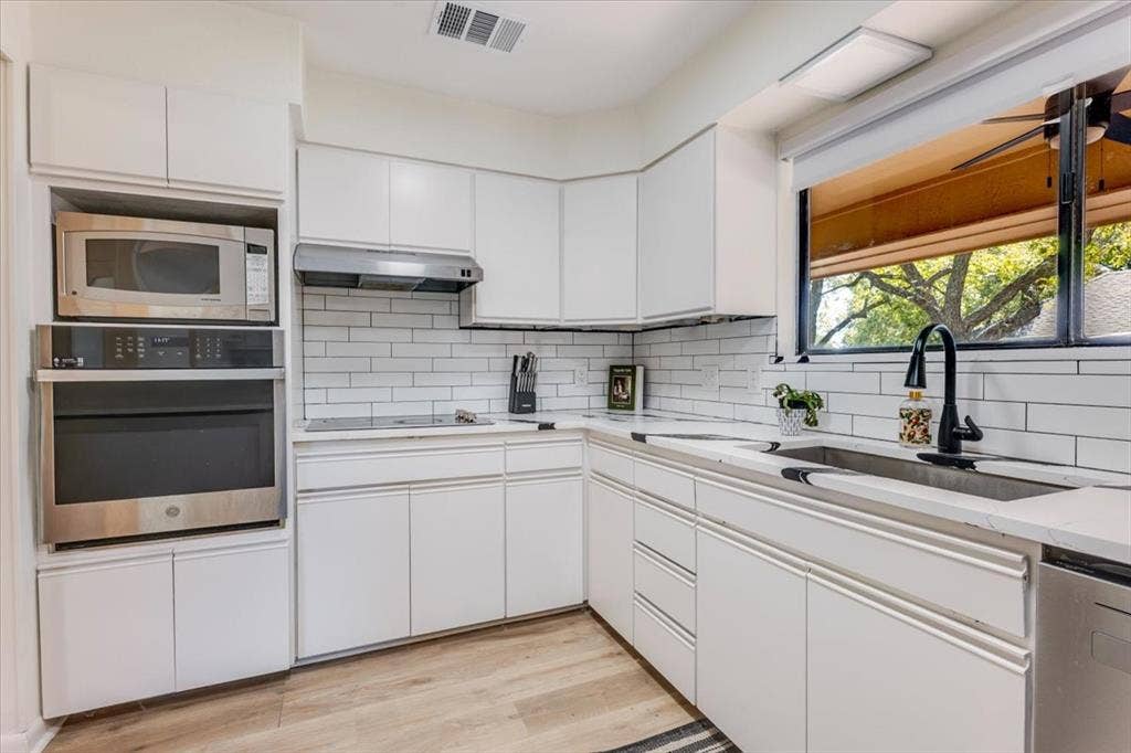 White cabinetry with integrated stainless steel appliances, subway tile backsplash, and light-toned countertops
