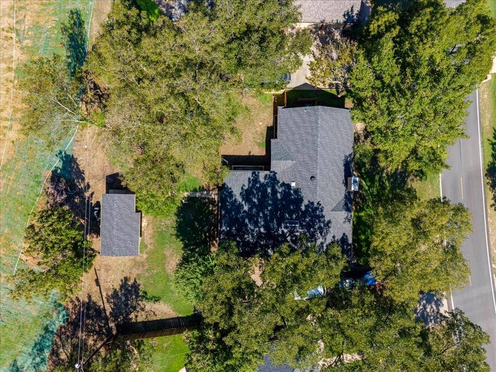 Property featuring a main residence with a dark shingle roof, a detached ancillary structure with a dark shingle roof, and mature trees on the premises