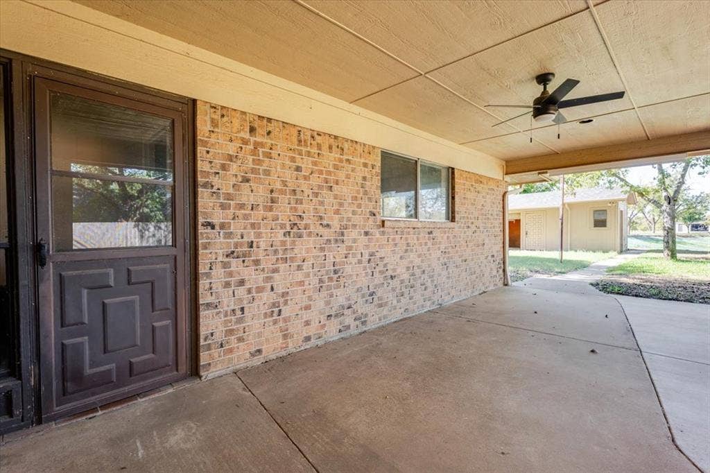 Expansive covered patio featuring a concrete surface, brick wall, and ceiling fan