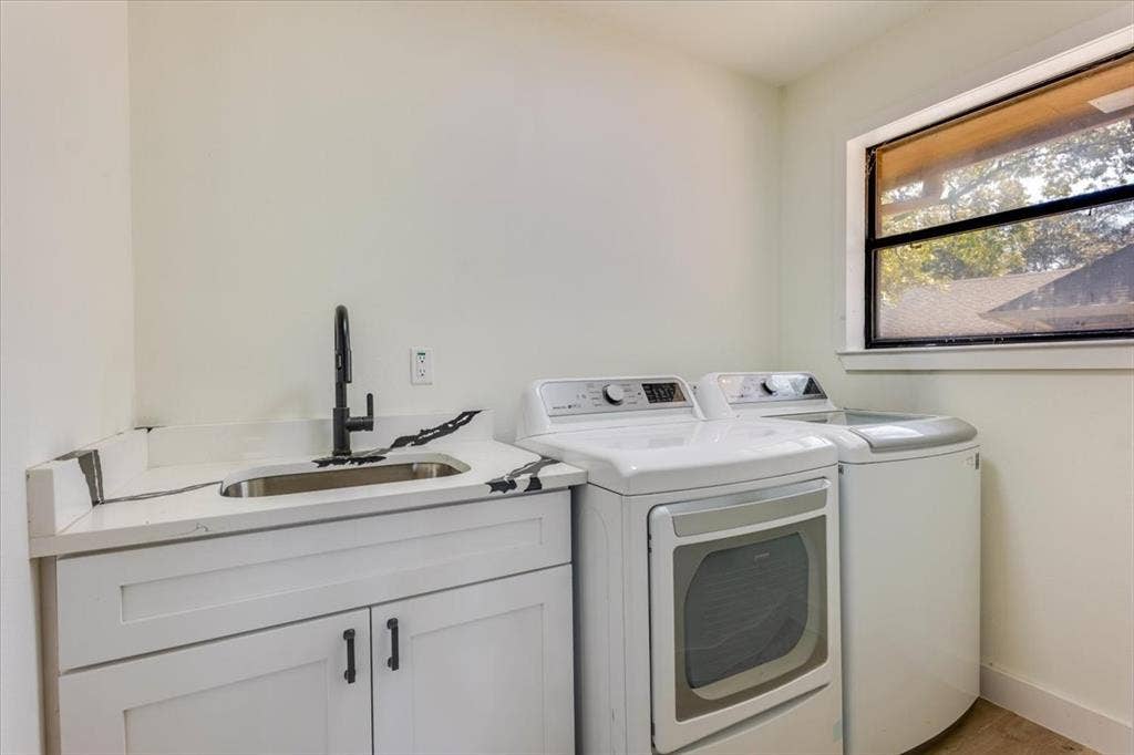 Laundry area featuring a utility sink with a matte black faucet, white cabinetry, and a window