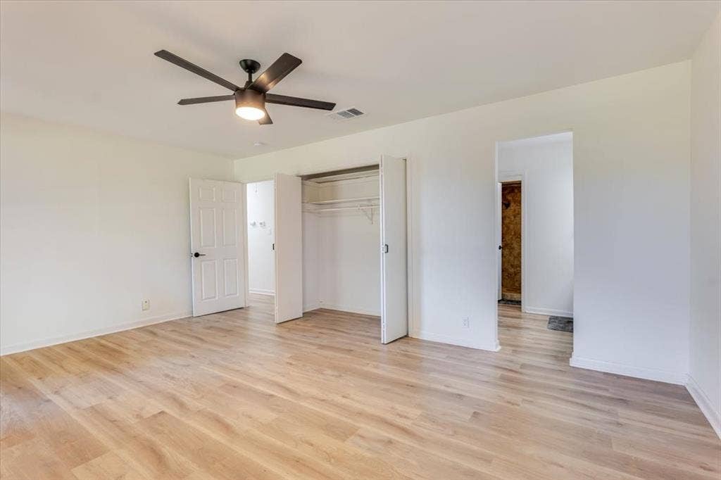 Expansive room featuring wood-finish flooring, a contemporary ceiling fan, and a built-in closet with bifold doors