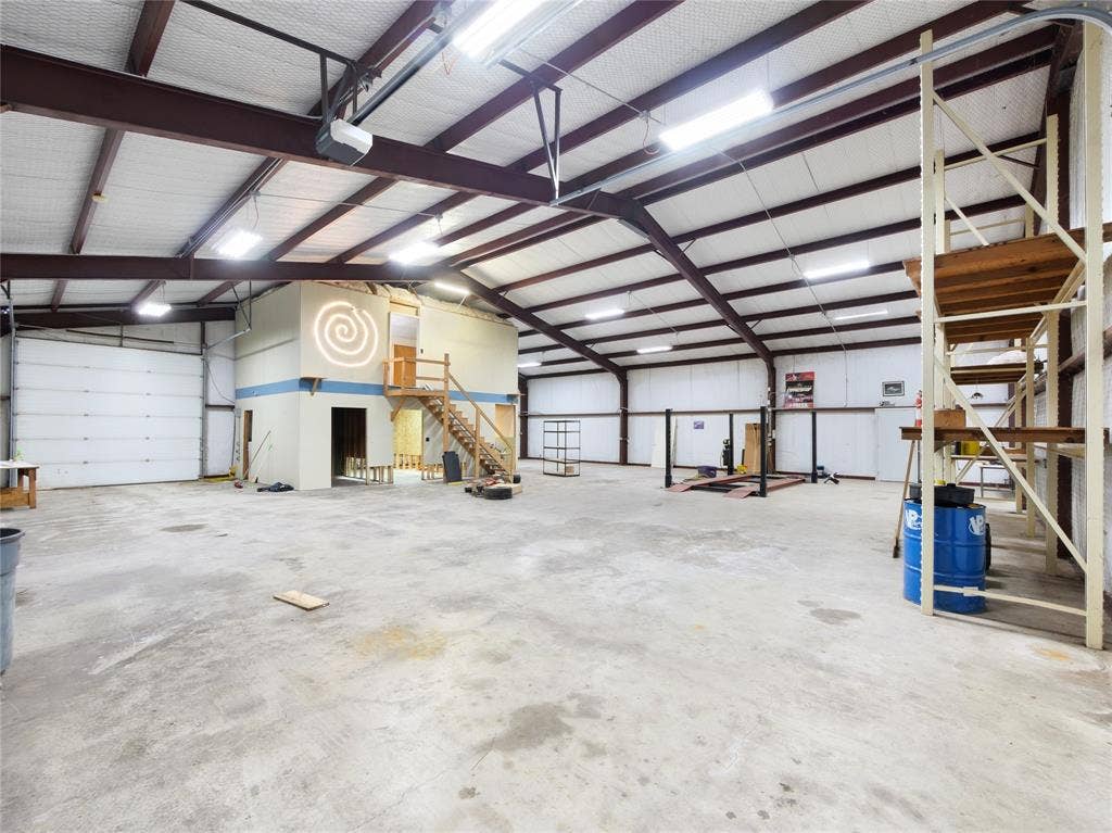 2944 CR-596, Nevada, TX 75173 Expansive industrial space featuring concrete flooring, exposed beam ceiling, multiple roll-up doors, and built-in shelving