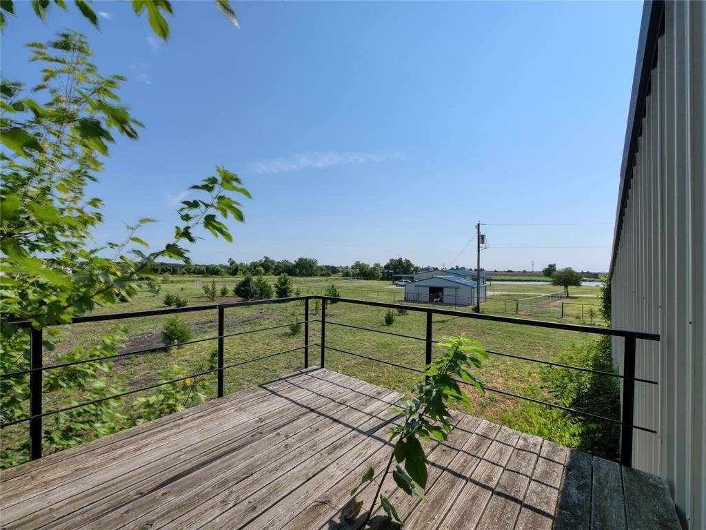 2944 CR-596, Nevada, TX 75173 Wood-finish deck with black metal railing, overlooking a green expanse and a distant outbuilding