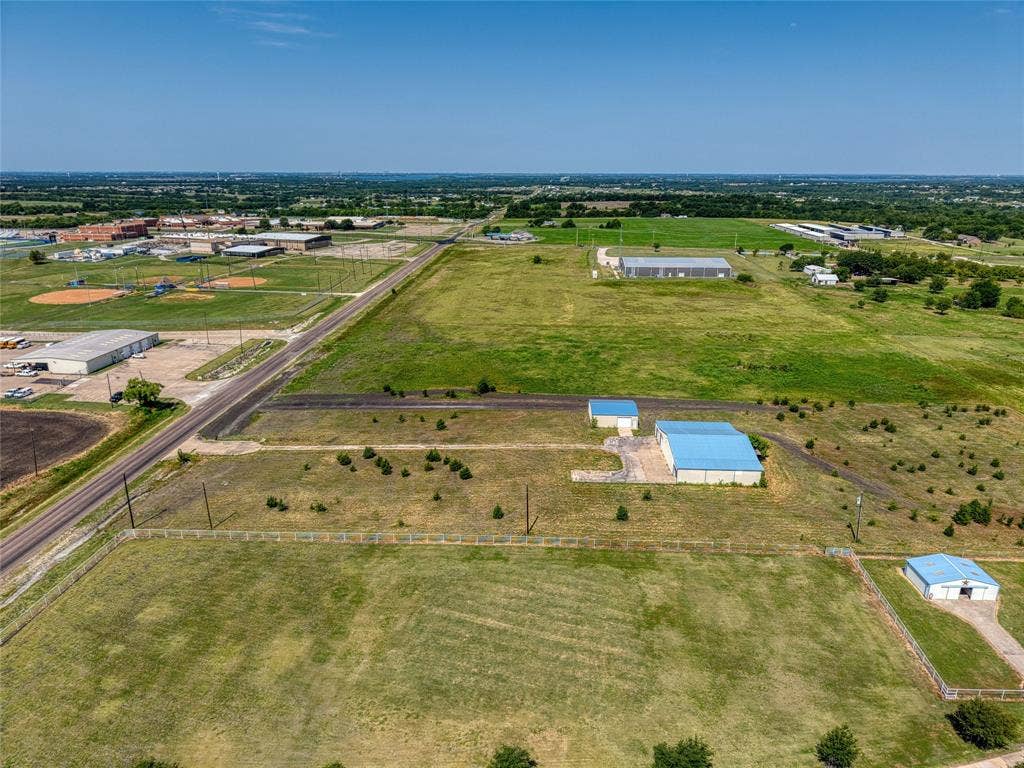 2944 CR-596, Nevada, TX 75173 Expansive acreage featuring multiple outbuildings with blue metal roofs, a lengthy paved driveway, and open fields