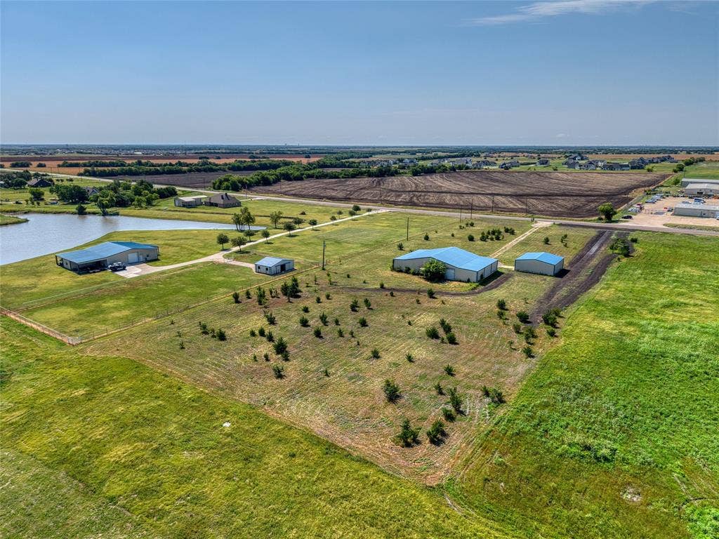 2944 CR-596, Nevada, TX 75173 Expansive property featuring a tranquil pond, multiple structures with blue metal roofing, and surrounding open land