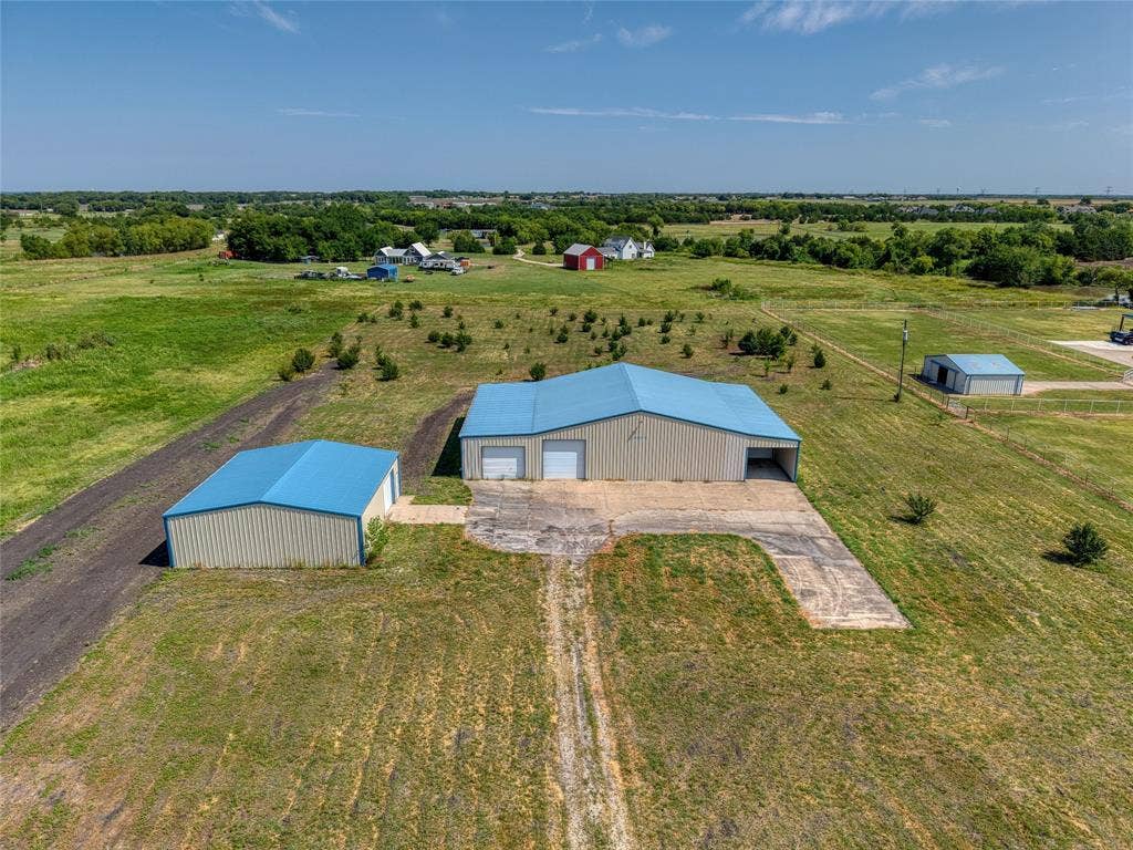 2944 CR-596, Nevada, TX 75173 Expansive property featuring a main metal building with a blue roof and multiple bay doors, a secondary metal building with a blue roof, and a gravel driveway