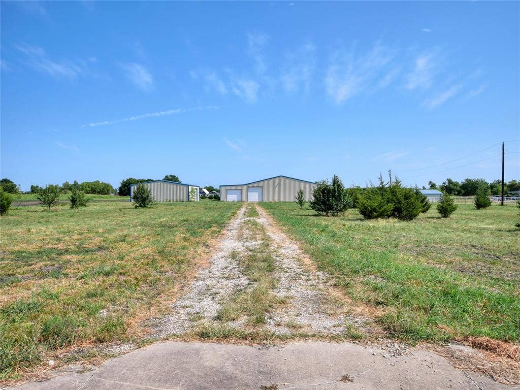 2944 CR-596, Nevada, TX 75173 Gravel drive approaching two metal buildings with roll-up doors, set within a grassy expanse
