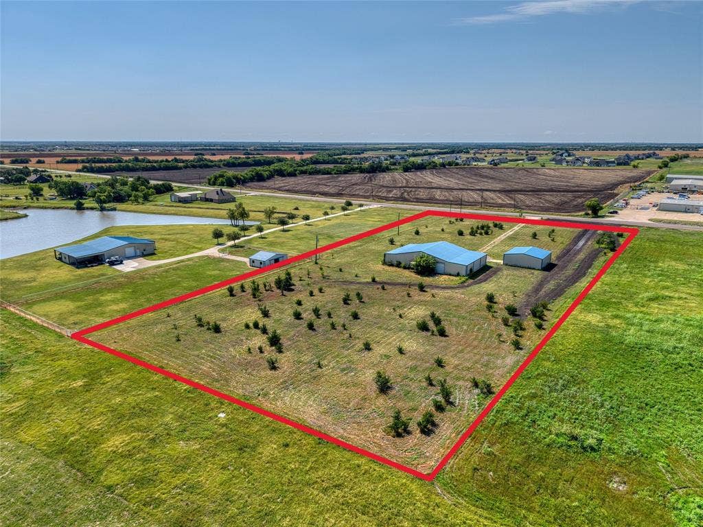 2944 CR-596, Nevada, TX 75173 Expansive lot featuring two metal-clad buildings with blue roofs, a smaller outbuilding, and scattered young trees