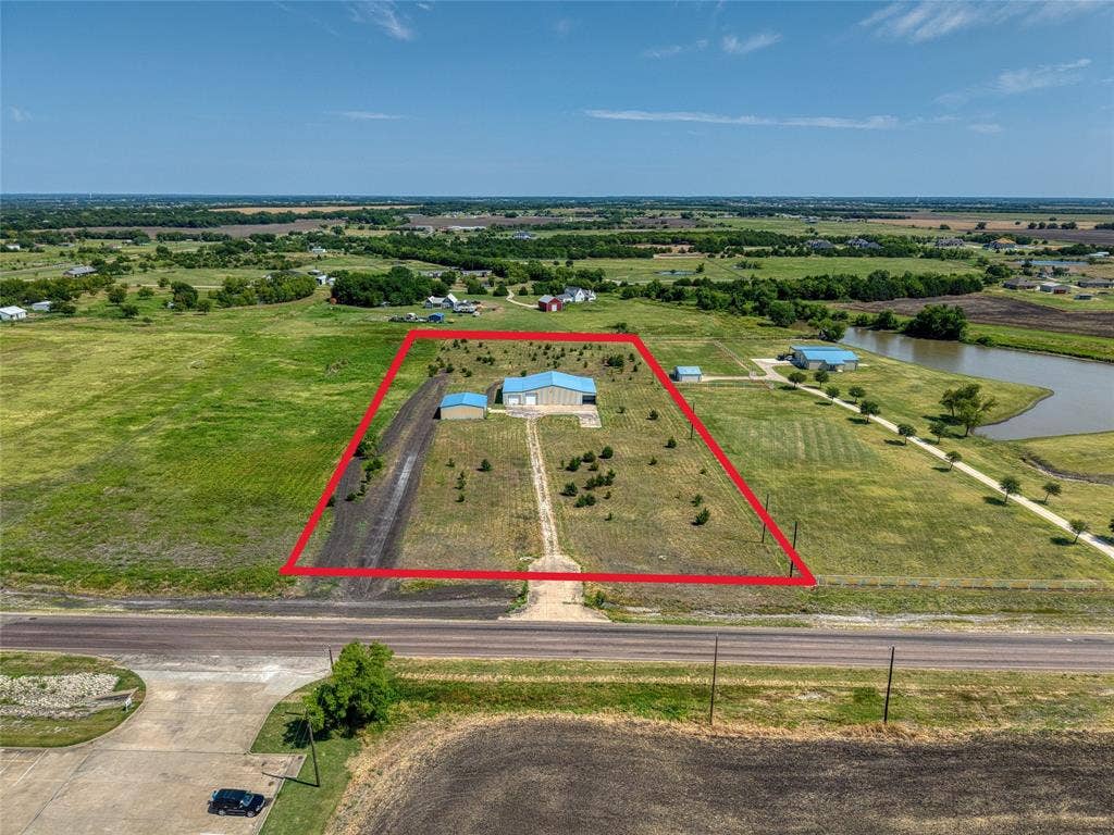 2944 CR-596, Nevada, TX 75173 Expansive rural acreage featuring a main building with a light blue roof, an additional outbuilding, and a clear access road from the highway