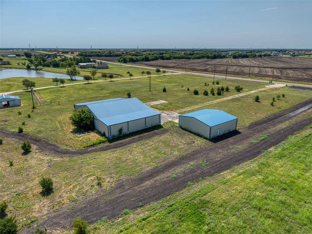 2944 CR-596, Nevada, TX 75173 Expansive rural property featuring two large metal-frame agricultural structures with blue metal roofing, situated on manicured grounds with newly planted landscaping