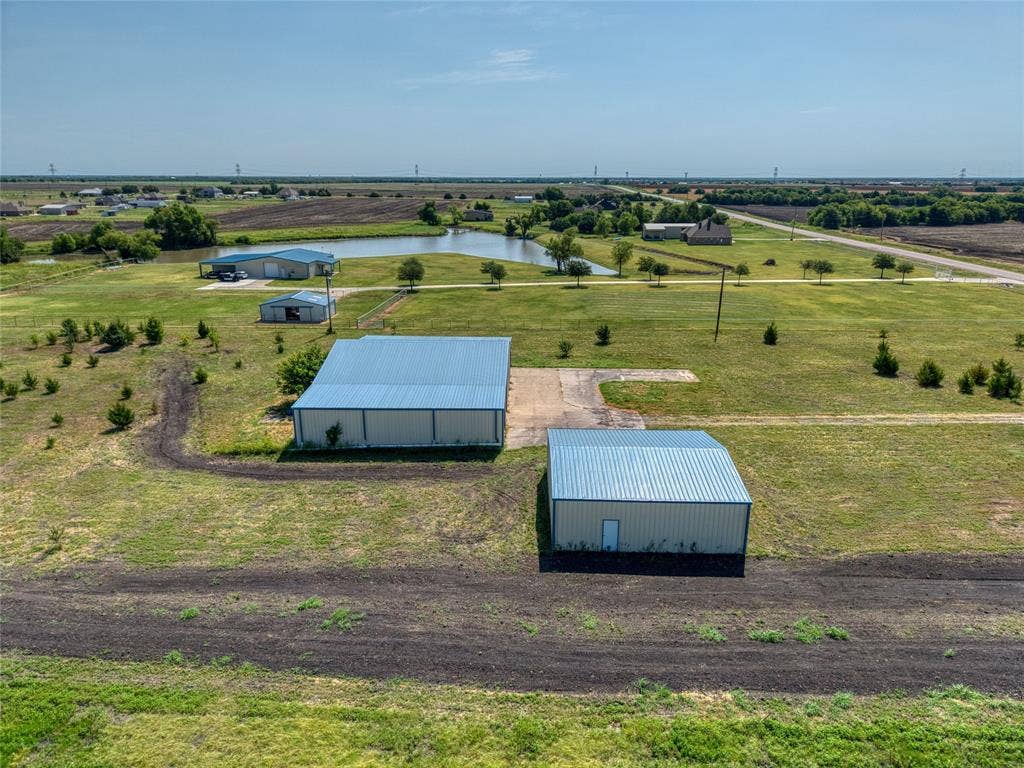 2944 CR-596, Nevada, TX 75173 Two metal buildings with light blue roofs, one larger and one smaller, are set on a property featuring a pond, a concrete pad, and an expanse of green lawn