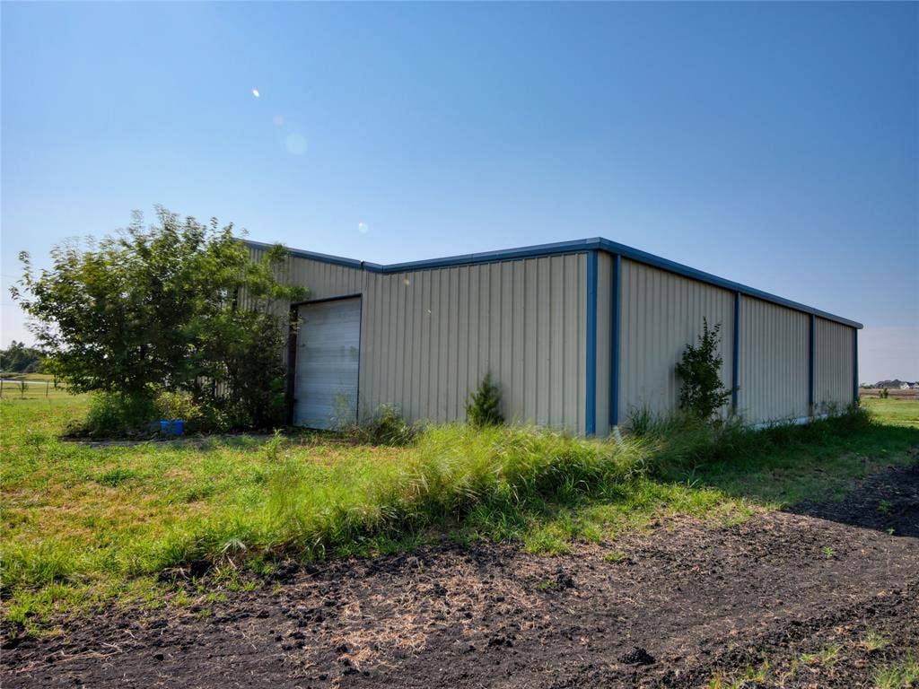 2944 CR-596, Nevada, TX 75173 Metal-sided outbuilding with blue trim, featuring a large roll-up door