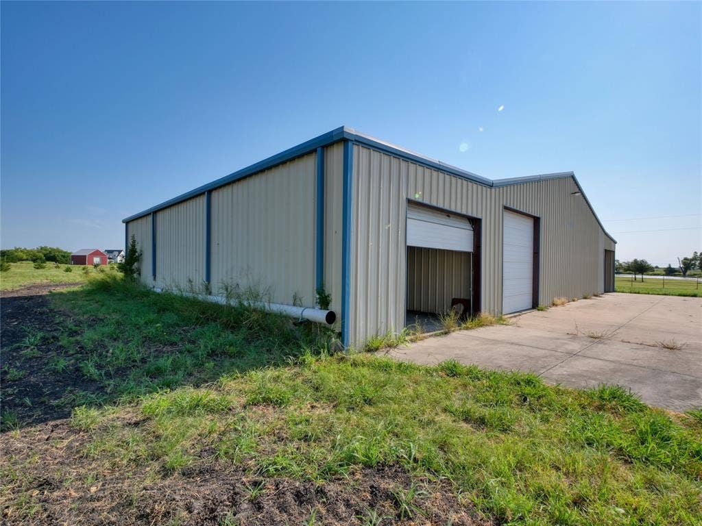 2944 CR-596, Nevada, TX 75173 Metal-sided building with multiple roll-up doors, a concrete drive, and a pitched roofline
