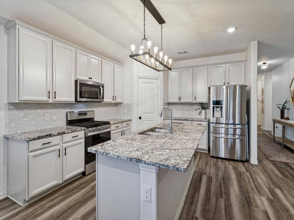 5513 Baker Creek Road, Fort Worth, TX 76126 Kitchen featuring a large center island with a stainless steel sink, wood-finish flooring, white cabinetry, stainless steel appliances, and a tiled backsplash
