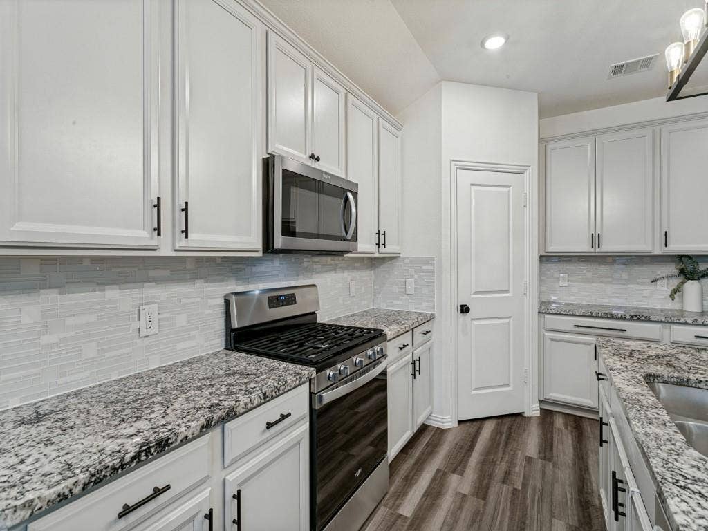 5513 Baker Creek Road, Fort Worth, TX 76126 White shaker-style cabinetry with black hardware, stainless steel range and microwave, light-toned backsplash, granite countertops, and wood-finish flooring