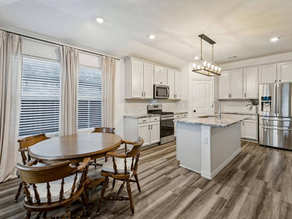 5513 Baker Creek Road, Fort Worth, TX 76126 Kitchen featuring white cabinetry, stainless steel appliances, a center island with a sink, wood-finish flooring, and recessed lighting