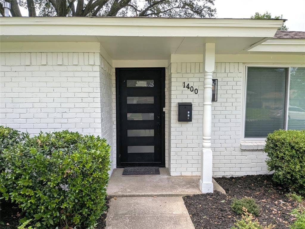1400 Oakhill Drive, Plano, TX 75075 White painted brick exterior with a modern black entry door featuring horizontal glass panels