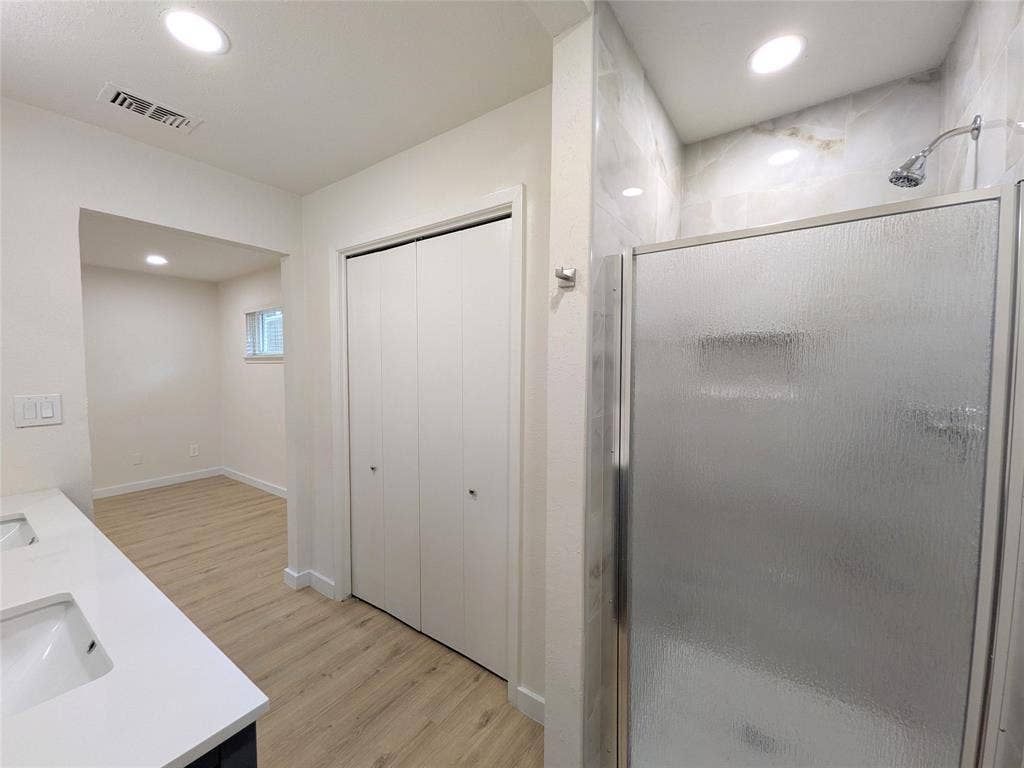 1400 Oakhill Drive, Plano, TX 75075 Spacious bathroom featuring a glass-enclosed shower with tiled walls, a dual-sink vanity with white countertops, bi-fold closet doors, and recessed lighting