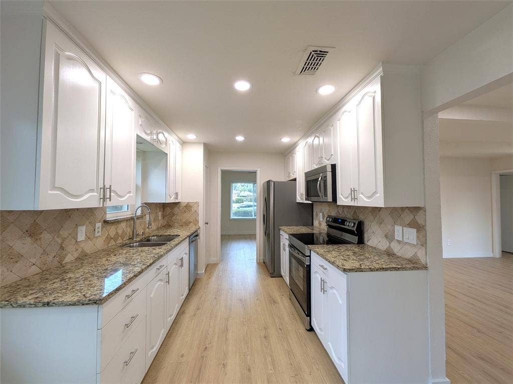 1400 Oakhill Drive, Plano, TX 75075 Galley kitchen featuring white cabinetry, granite-finish countertops, stainless steel appliances, a tile backsplash, and wood-finish flooring