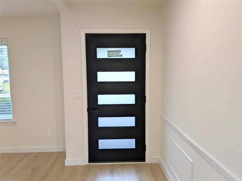 1400 Oakhill Drive, Plano, TX 75075 Contemporary entry door with frosted glass panels, matte black hardware, light wood-finish flooring, and decorative wainscoting