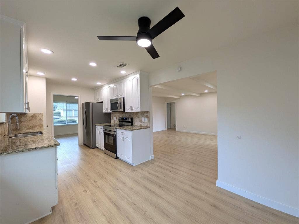 1400 Oakhill Drive, Plano, TX 75075 Kitchen featuring wood-finish flooring, white cabinetry, granite countertops, stainless steel appliances, and a tiled backsplash
