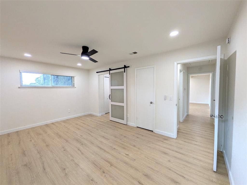 1400 Oakhill Drive, Plano, TX 75075 Spacious room featuring wood-finish flooring, a modern black ceiling fan, recessed lighting, and a sliding barn door with frosted glass panels