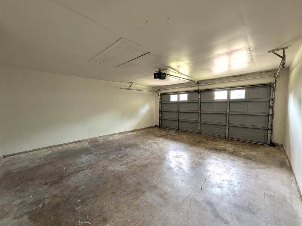 1400 Oakhill Drive, Plano, TX 75075 Interior garage space featuring a grey sectional garage door with upper window inserts, an automatic garage door opener, and a ceiling access panel