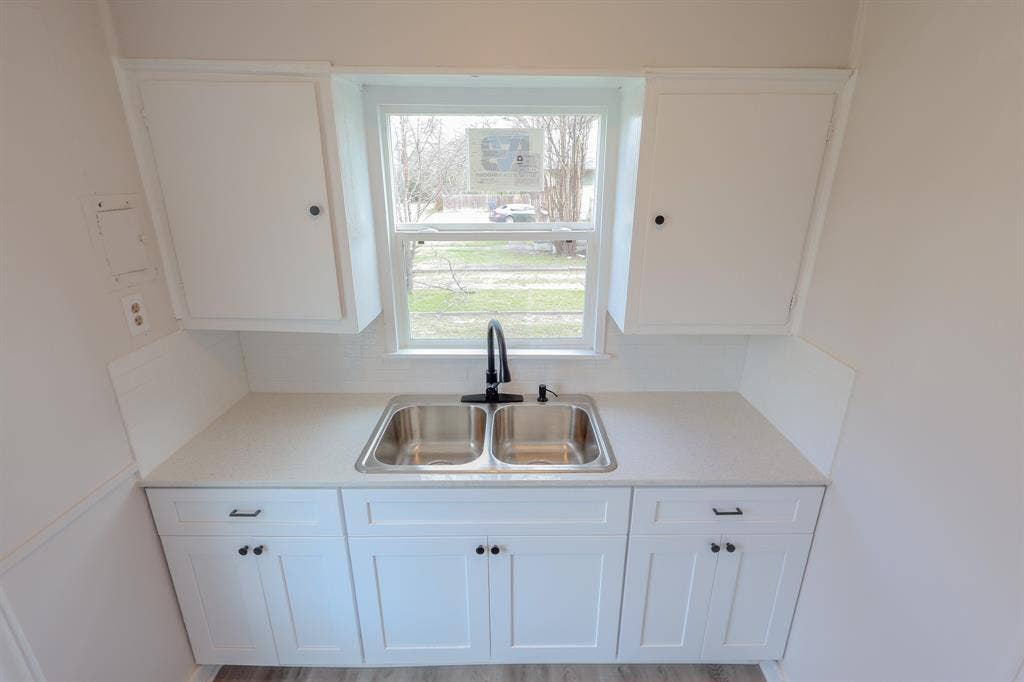 1704 Ethel Avenue, #B, Waco, TX 76707 White cabinetry with black hardware, solid surface countertop, stainless steel double basin sink, and black gooseneck faucet