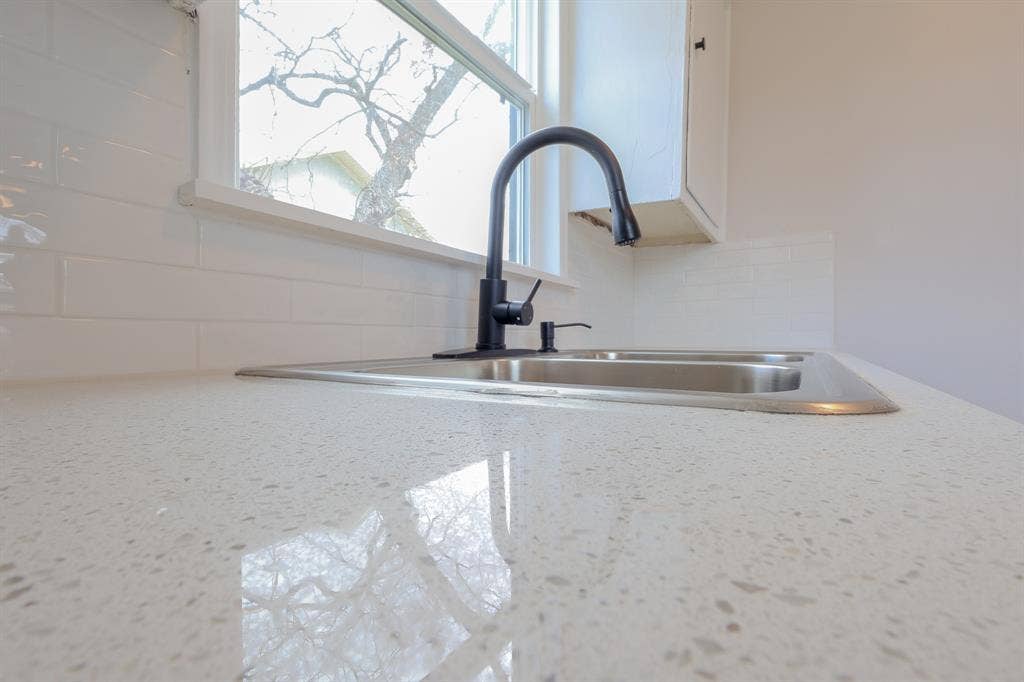 1704 Ethel Avenue, #B, Waco, TX 76707 Polished stone-finish countertop, stainless steel double basin sink, matte black gooseneck faucet, and white subway tile backsplash
