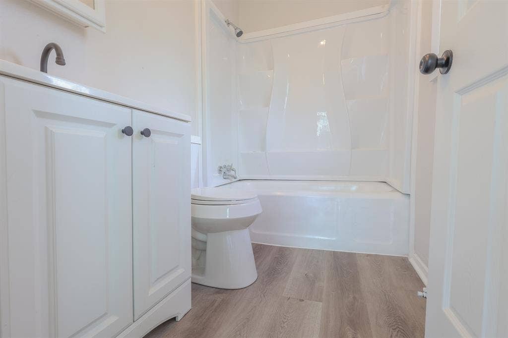 1704 Ethel Avenue, #B, Waco, TX 76707 White vanity with dark hardware, white toilet, white tub-shower combination, and wood-finish flooring