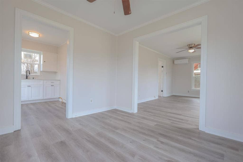1704 Ethel Avenue, #B, Waco, TX 76707 Light wood-finish flooring throughout, white walls with crown molding, white kitchen cabinetry with a dark faucet, and a ceiling fan